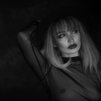 Black White Aufnahme von einer blonden Frau mit dunklen Lippen. Der Hintergrund ist verschwommen. Es kommt nur ihr Gesicht scharf raus und sie sieht nachdenklich nach links.