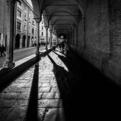 Black White Aufnahme einer Innenstadt in Italien. Der Blick liegt auf einem Bogengang mit Kopfsteinplaster.