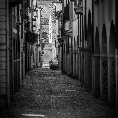 Black White Aufnahme einer Gasse in Italien mit alten Häusern, Kopfsteinpflaster und einer Kirche im Hintergrund.