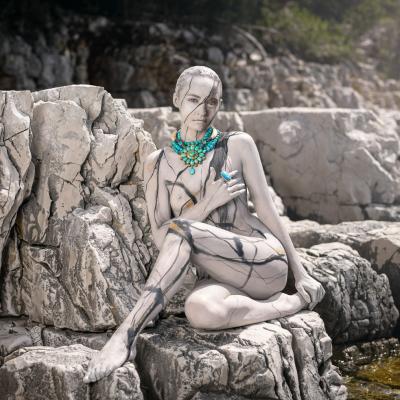 Frau mit Camouflagebemalung posiert mit bunter Kette vor Felsen