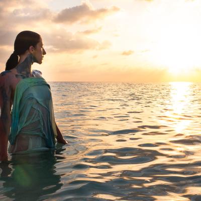 Frau steht im Meer und beobachtet Sonnenuntergang