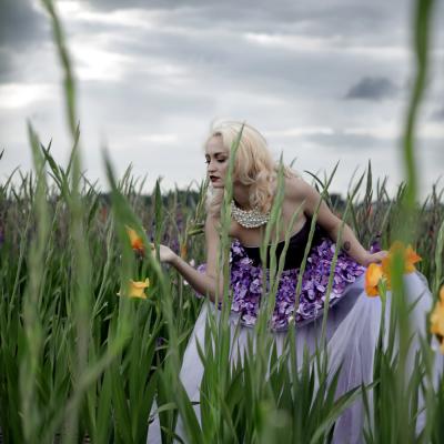 Blonde Frau mit rosa Prinzessinnenkleid steht in buntem Blumenfeld