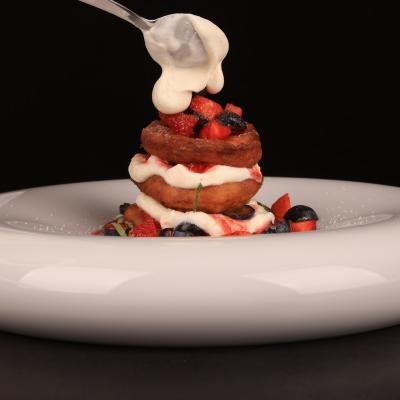 weißer gebogener Teller mit Pancakes geschichtet mit roten Früchten und Joghurt
