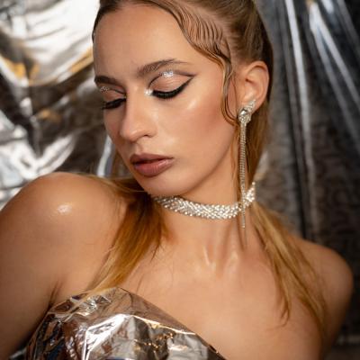 Frau mit glamourösem Make-up und Schmuck vor metallischem Hintergrund im Studio