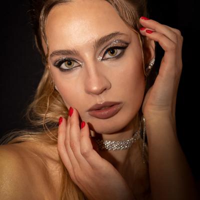 Nahaufnahme einer Frau mit elegantem Make-up und Schmuck vor dunklem Hintergrund