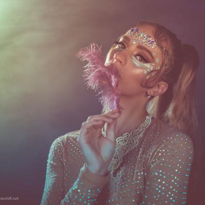 Frau mit kreativem Make-up und Feder vor farbigem Studiohintergrund
