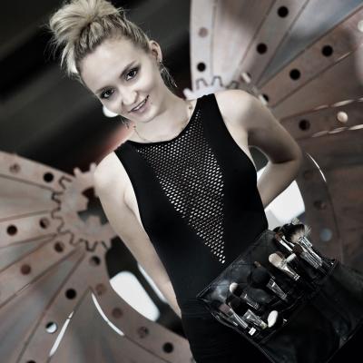 Visagistin Anna Barendregt mit Make-up-Pinseln posiert in modernem Studio mit industriellem Hintergrund